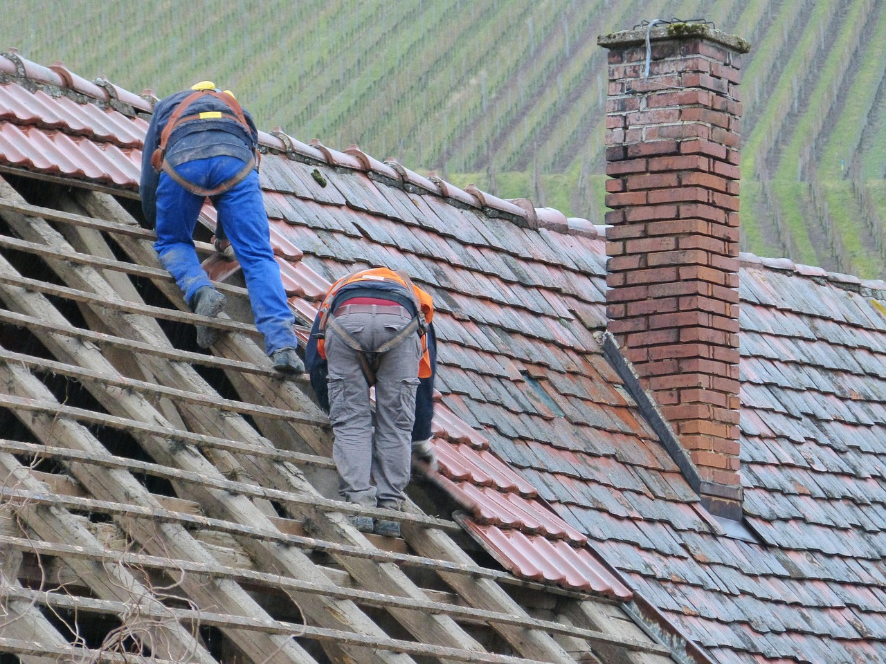 Two roofers stripping old tiles beside a brick chimney with lead flashing